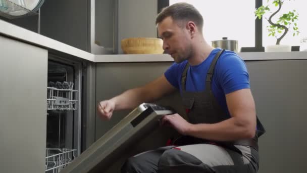 El capataz en uniforme fija la puerta del lavavajillas en la cocina — Vídeo de stock