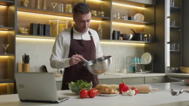 Genç adam yemek pişiriyor. Yemek tarifini bilgisayarda izliyor.