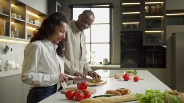 Casal jovem corta verduras para salada na cozinha em casa — Vídeo de Stock