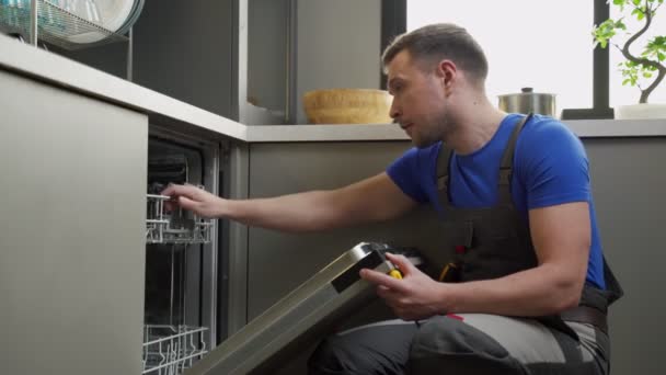 Tamirci mutfakta tornavidayla bulaşık makinesini tamir ediyor. — Stok video