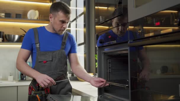 Doświadczony brygadzista naprawia piekarnik śrubokrętem w kuchni — Wideo stockowe