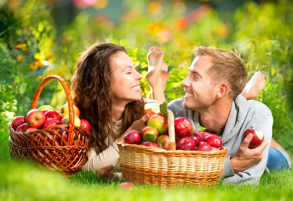 Pareja Relajarse en la hierba y comer manzanas en el jardín de otoño —  Fotos de Stock