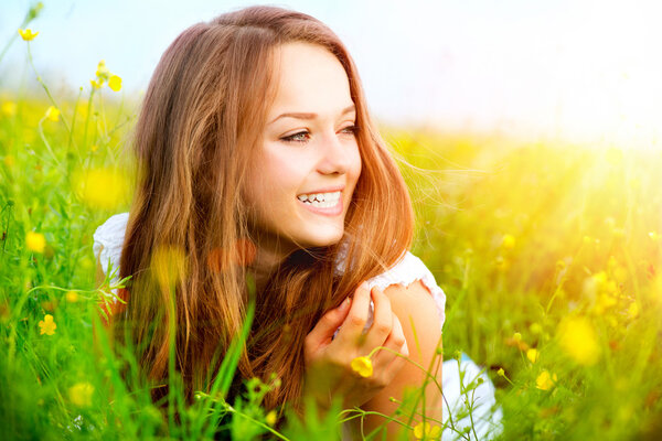 Beauty Girl in the Meadow lying on Green Grass with wild Flowers