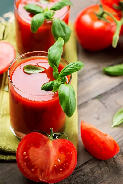 Tomatensaft und frische Tomaten mit Basilikum auf einem Holztisch — Stockfoto