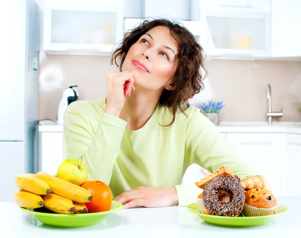 Dietkonceptet. Ung kvinna väljer mellan frukt och sötsaker — Stockfoto