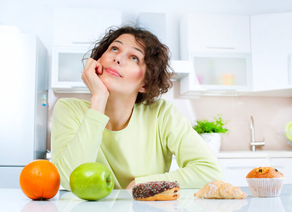 Dieting concept. Young Woman choosing between Fruits and Sweets