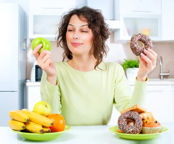 Concepto de dieta. Mujer joven eligiendo entre frutas y dulces —  Fotos de Stock