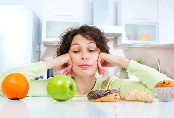 Dieting concept. Young Woman choosing between Fruits and Sweets Stock Picture