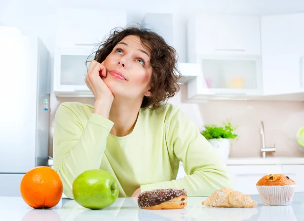 Dieting concept. Young Woman choosing between Fruits and Sweets Stock Image