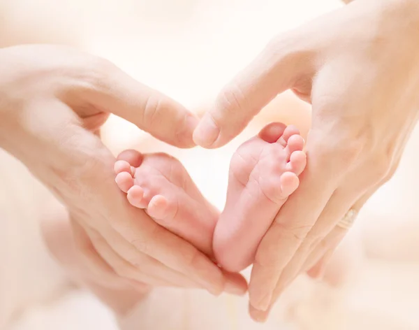 Pequenos pés de bebê recém-nascido no coração feminino em forma de mãos close-up — Fotografia de Stock