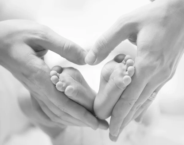 Klein pasgeboren baby's voeten op vrouwelijke hart gevormde handen close-up — Stockfoto