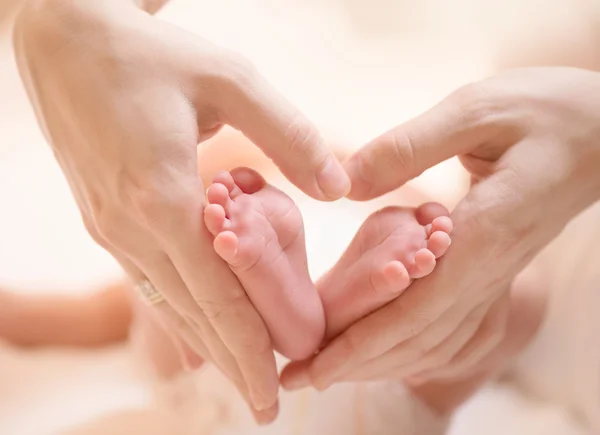 Pequenos pés de bebê recém-nascido no coração feminino em forma de mãos close-up — Fotografia de Stock