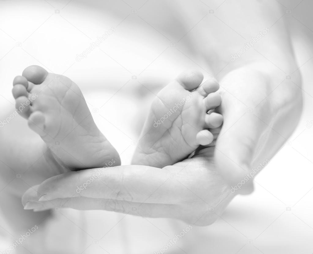 Tiny Newborn Baby's feet on female hands closeup