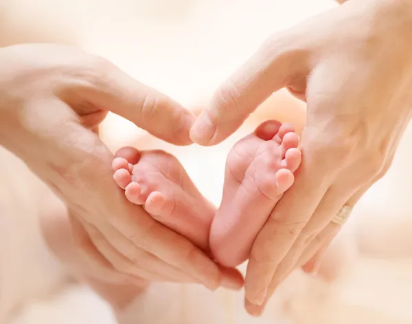 Pequenos pés de bebê recém-nascido no coração feminino em forma de mãos close-up — Fotografia de Stock