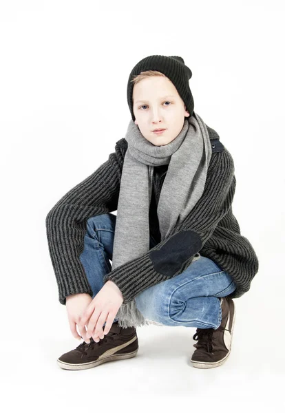 Boy in a cap and a scarf sitting on a white background — Stock Photo, Image