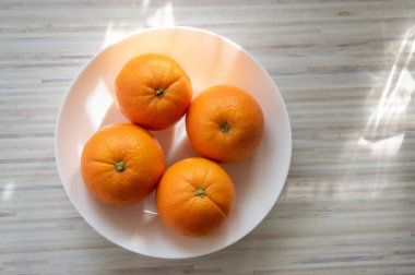 Dört portakallı bir grup portakal beyaz tabakta beyaz tabakta güneş ışığında çiğ, sağlıklı meyveler.