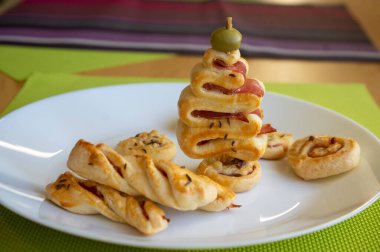 Peynirli, jambonlu ve yeşil zeytinli tuzlu pasta fırını, Noel ağacı, çubuklar ve yuvarlak şekilli beyaz tabaklar.