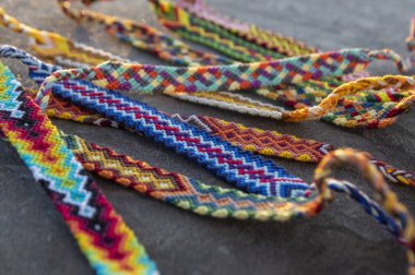 El yapımı, renkli, doğal, örülmüş arkadaşlık bilezikleri. Gri donmuş arka planda, parlak renkler.