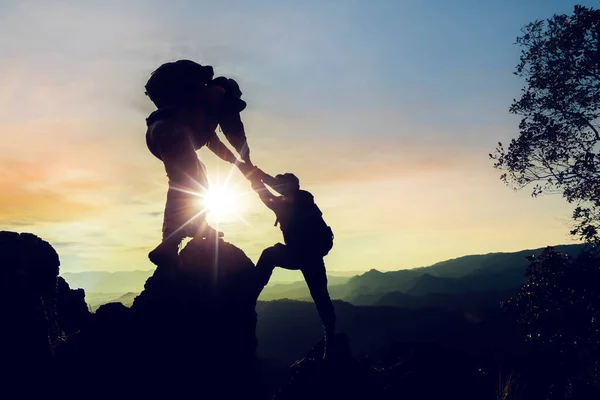 Silhouette climbing buddies help each other climb up the mountain at sunrise as the right lifestyle idea