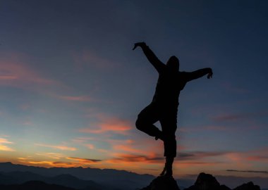 Doğada gün batımı ve altın gökyüzü ile yoga yapan adamın fotoğrafı. Tek bacaklı bir adam kayaların üzerinde duruyor.