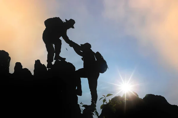 Silhouette of two people climbing a mountain in a trekking activity at sunset, teamwork assistance concept