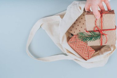 Çocuk kumaş trend çantasından organik Noel hediyelerini alıyor gri arka planda süslü çalı çırpı dalları. Düz yerde, üst tarafta. Yüksek kalite fotoğraf