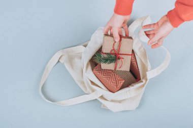 Çocuk kumaş trend çantasından organik Noel hediyelerini alıyor gri arka planda süslü çalı çırpı dalları. Düz yerde, üst tarafta. Yüksek kalite fotoğraf