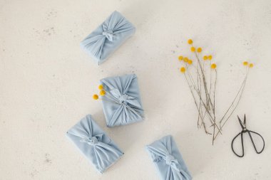 Composition of eco gifts wrapped in blue reusable fabric and craspedia globosa dry flowers for decoration. on a white table. High quality photo clipart