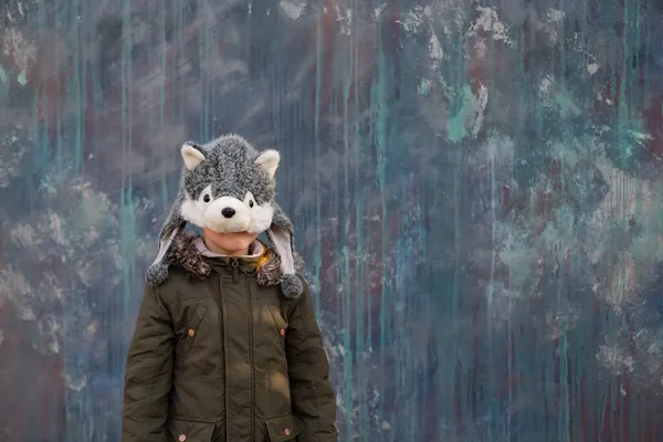 El niño escondido detrás de un sombrero de lobo sobre fondo gris, al aire libre. espacio para texto — Foto de Stock