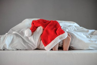 Noel Baba şapkasıyla yatağın üzerinde çocuk ayakları. Yılbaşı ve Noel 'de evdeyiz. İyi tatiller. Metin için boşluk. Yüksek kalite fotoğraf