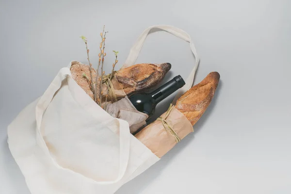 Eco bag, baked french bread, bottle of wine and glasses on a gray background. Christmas sustainable lifestyle concept. top view. High quality photo