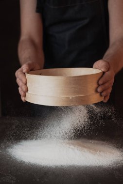 Cooking, kneading dough. Male hands sift flour onto the dough on a dark background. High quality photo