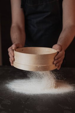 A dark background baker's hands sift white wheat flour over a sieve over. High quality photo