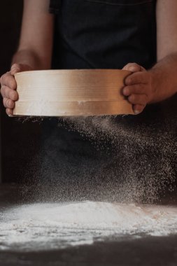 A dark background baker's hands sift white wheat flour over a sieve over. High quality photo