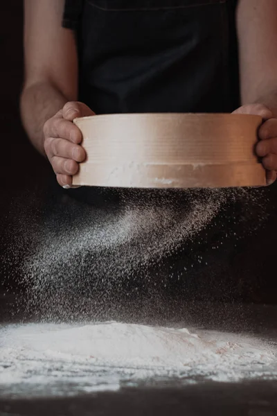 Men's hands are sifting flour through a sieve on black background. High quality photo