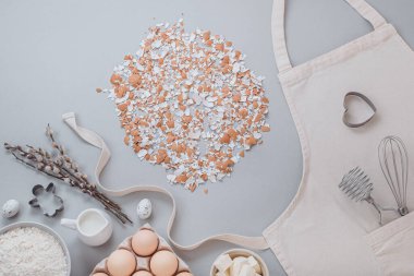 Düz konum kırık yumurta kabuğu ve pişirme malzemeleri ve gri arka planda mutfak aletleri. Bahar ve Paskalya kavramı, üst görünüm, metin için boşluk