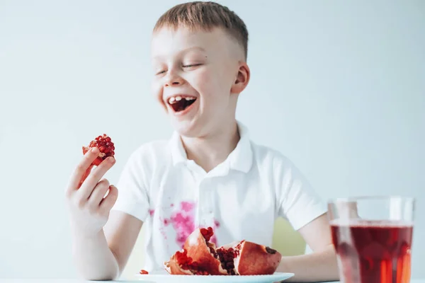 Barnens hand håller bit ett granatäpple och ler brett sitter vid bordet. begreppet smutsiga fläckar på kläder — Stockfoto