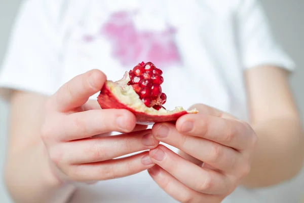 Uzavřete plátek semínek granátového jablka v rukou dítěte. špinavá skvrna granátového jablka šťáva po otevření na oblečení na pozadí — Stock fotografie