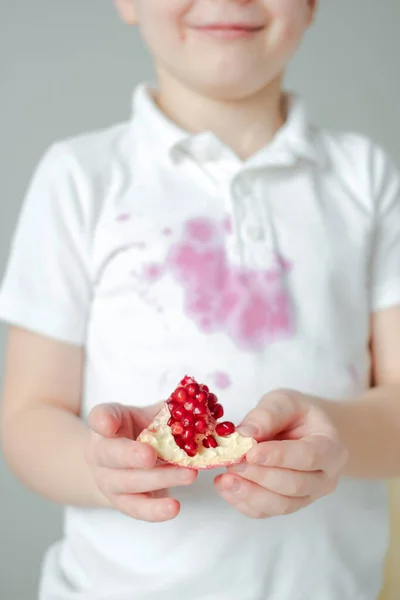 Uzavřete plátek semínek granátového jablka v rukou dítěte. špinavá skvrna granátového jablka šťáva po otevření na oblečení na pozadí — Stock fotografie