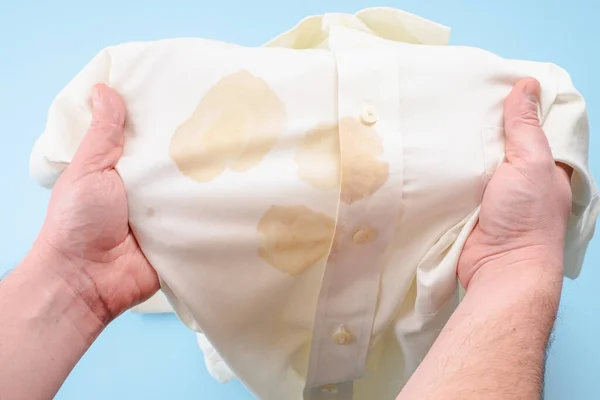 Manos de hombre sosteniendo una camisa con una mancha sucia de comida. mancha de salsa de soja en la camisa. aislado sobre fondo azul. vista superior — Foto de Stock