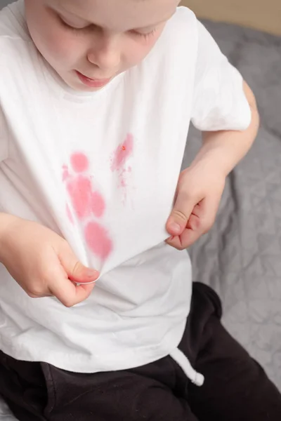 Child showing dirty stain on his white t-shirt. The concept of cleaning stains on clothes. — Stock Photo, Image