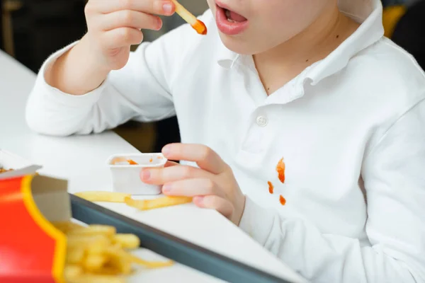 把白色童装上肮脏的番茄酱污迹清理干净男孩在快餐店里吃薯条、薯片和番茄酱。孩子们吃不健康的脂肪食物. — 图库照片