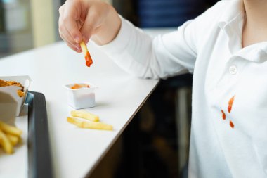 Beyaz çocuk kıyafetlerindeki kirli ketçap lekelerini kapat. Fast food restoranında patates cipsi ve domates sosu yiyen çocuk. Çocuklar sağlıksız yağlı yiyecekler yerler. Yüksek kalite fotoğraf
