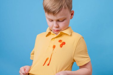 Çocuk, tişörtünde domates sosu ve spagetti yemeği lekesi gösteriyor. Kıyafetlerdeki leke temizleme konsepti. Yüksek kalite fotoğraf