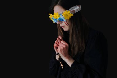 Kafasında çelenk olan üzgün bir kadın elinde bir tespihle arka planda dua ediyor. Ukrayna 'da Savaş