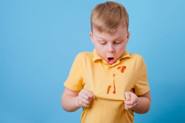 Çocuk, tişörtünde domates sosu ve spagetti yemeği lekesi gösteriyor. Kıyafetlerdeki leke temizleme konsepti. Yüksek kalite fotoğraf