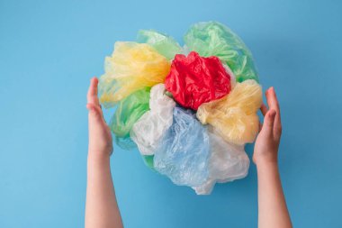 Çocukların elleri mavi arka planda plastik torbalar ve farklı renklerde plastik ambalajlar tutuyor. Üst Manzara. Yüksek kalite fotoğraf