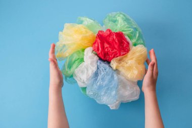 children's hands holding a set of plastic bags and plastic wraps of different colors on a blue background. top view. High quality photo clipart