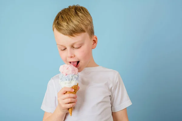 Positive boy licking ice cream on a blue background. Health benefits ice cream concept. High quality photo