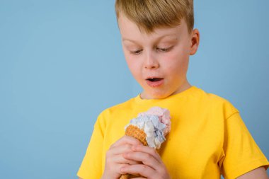 Pozitif çocuk mavi arka planda dondurma yalıyor. Sarı elbiseli kirli dondurma lekesi. Günlük yaşam lekesi ve temizlik konsepti 
